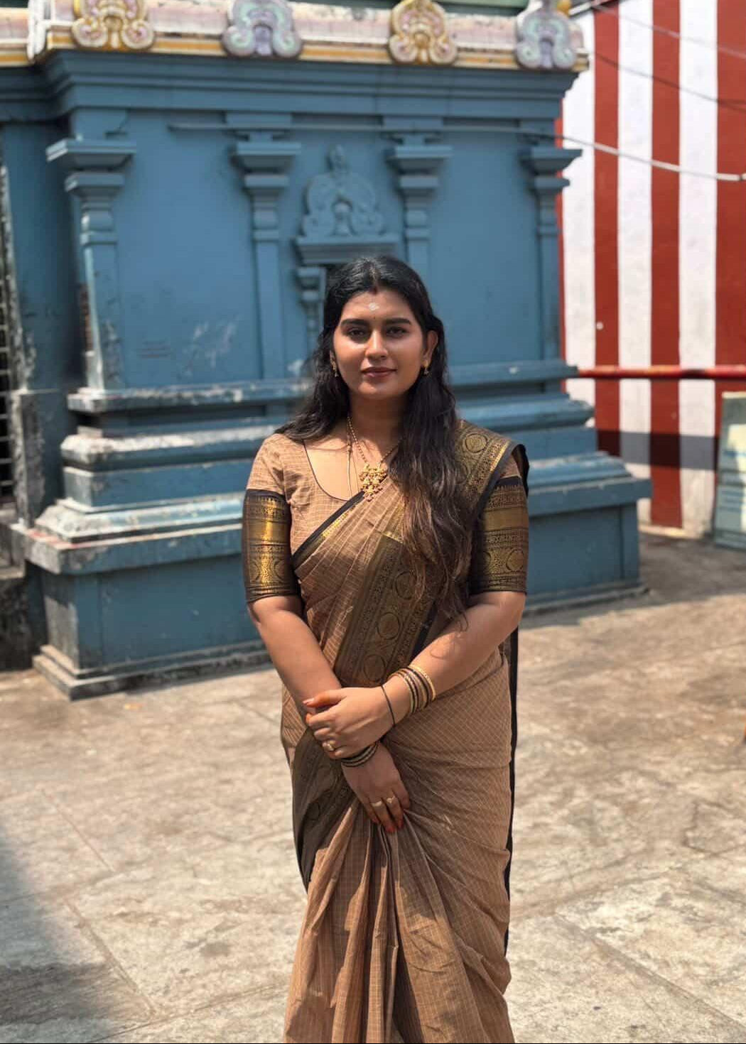 Woman in a traditional saree standing in front of a temple structure.